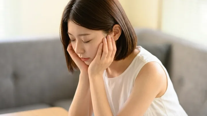 借金の返済に悩み、頬に手を当てて考え込む女性